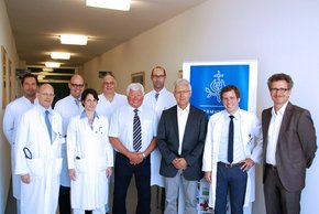 v.l.n.r. Facharzt Dr. Filip Kostal, Chefarzt Prof. Dr. Cornel Sieber, Oberarzt Dr. Michael Winter, Leitende Ärztin Privatdozentin Dr. Ute Hoffmann, Leitender Oberarzt Dr. Bernhard Fichtl, Oberarzt Dr. Gerhard Herzog (alle Klinik für Innere Medizin und G (Krankenhaus Barmherzige Brüder Regensburg) man sieht viele Männer, 2 davon in Anzügen und der Rest in Kitteln. Sie stehen lächelnd vor dem Logo der BB